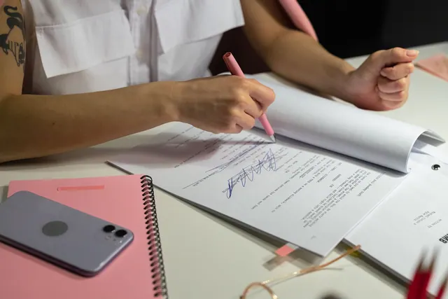 Close-up of a person writing on documents at a well-organized office desk. Grants for women checklist: documents and steps