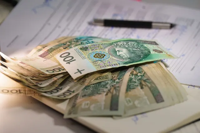 Stack of Polish zloty banknotes on financial documents with a pen, indicating monetary transactions in an office setting. Local grants: costs, choices and current rules